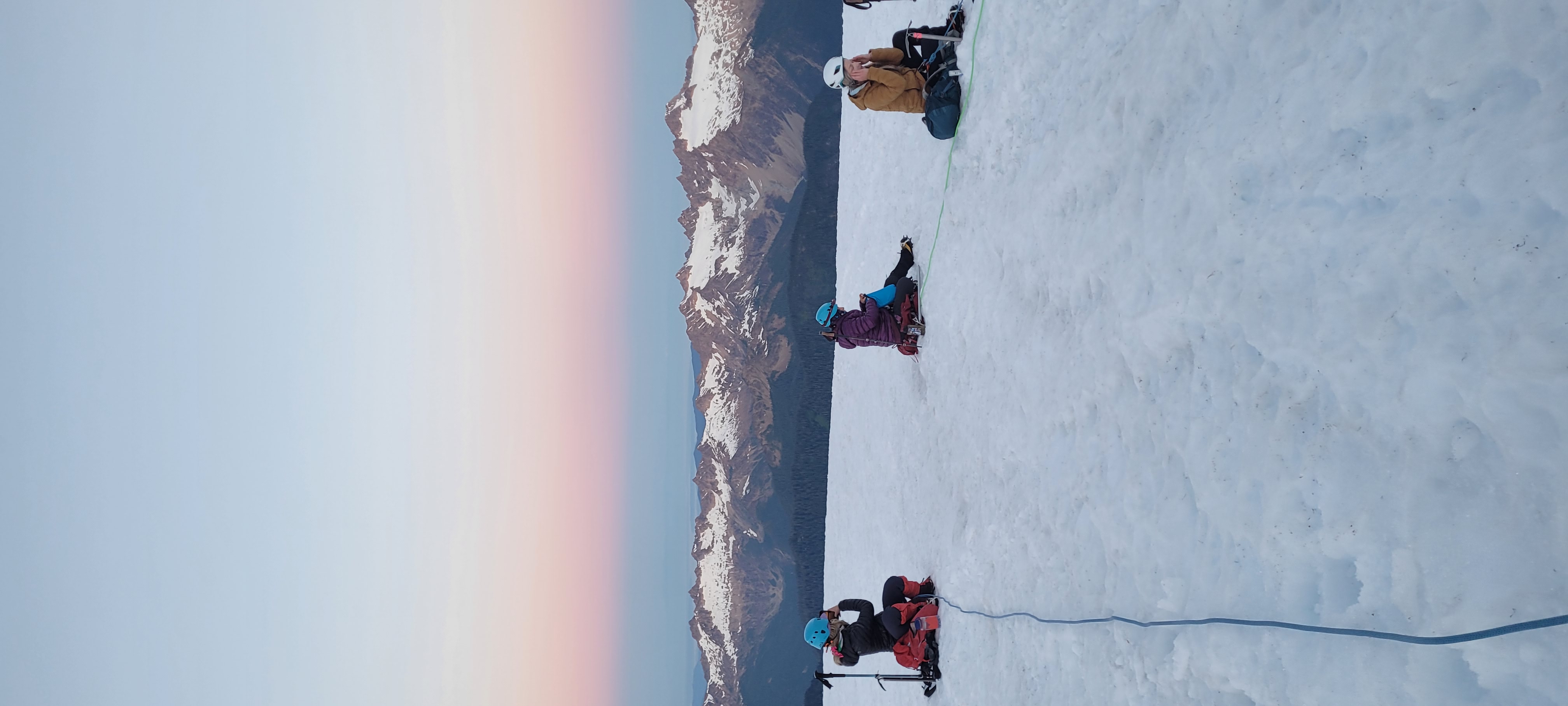 Climbers roped together on the glacier at sunrise, Cascades visible below
