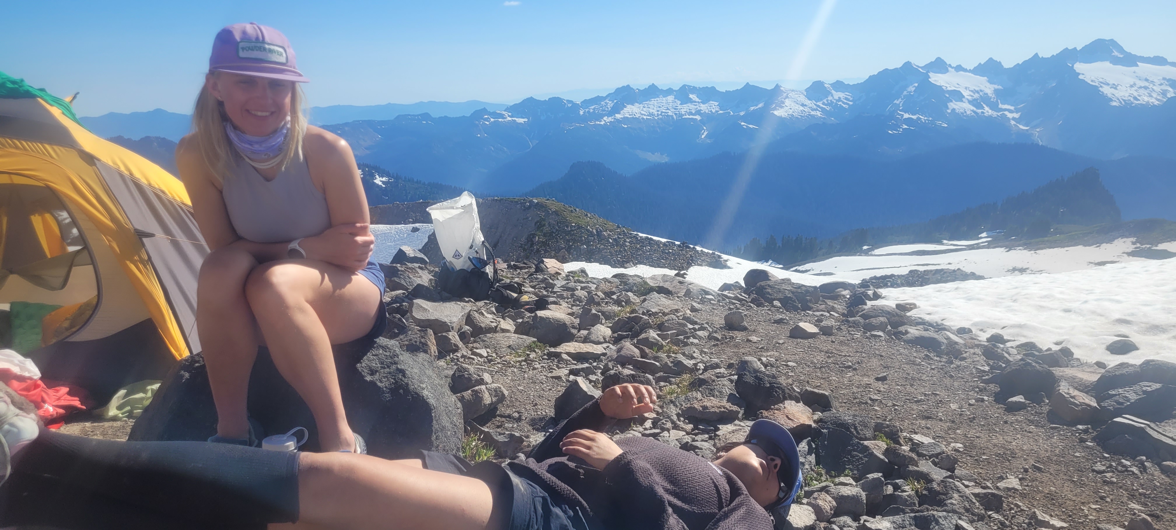 Two people resting at high camp — tent, rocks, Cascades panorama spread out behind