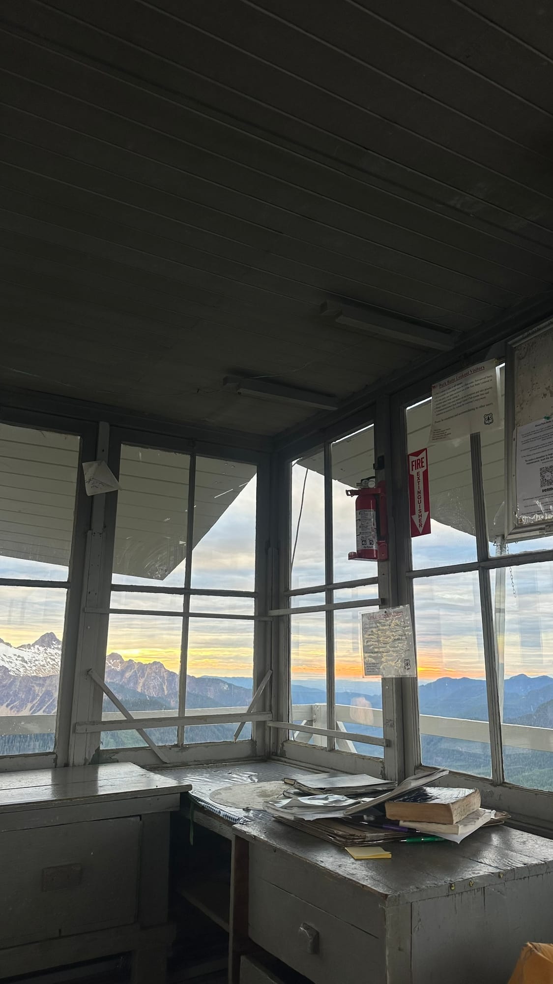 Inside the lookout at sunrise, orange sky through the windows, fire extinguisher and logbooks