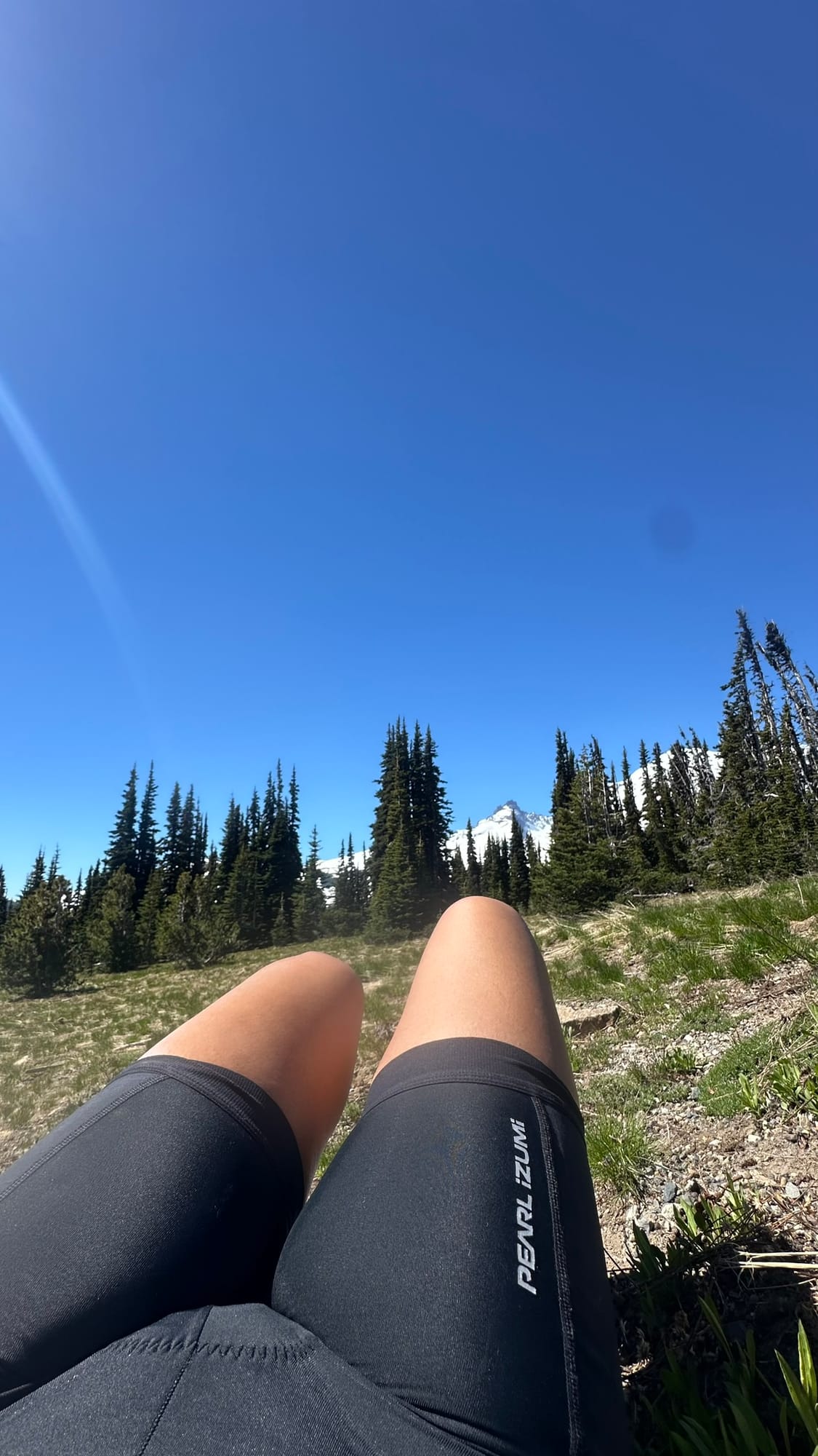 Legs in Pearl Izumi bibs lying back in meadow grass with Rainier close and large behind
