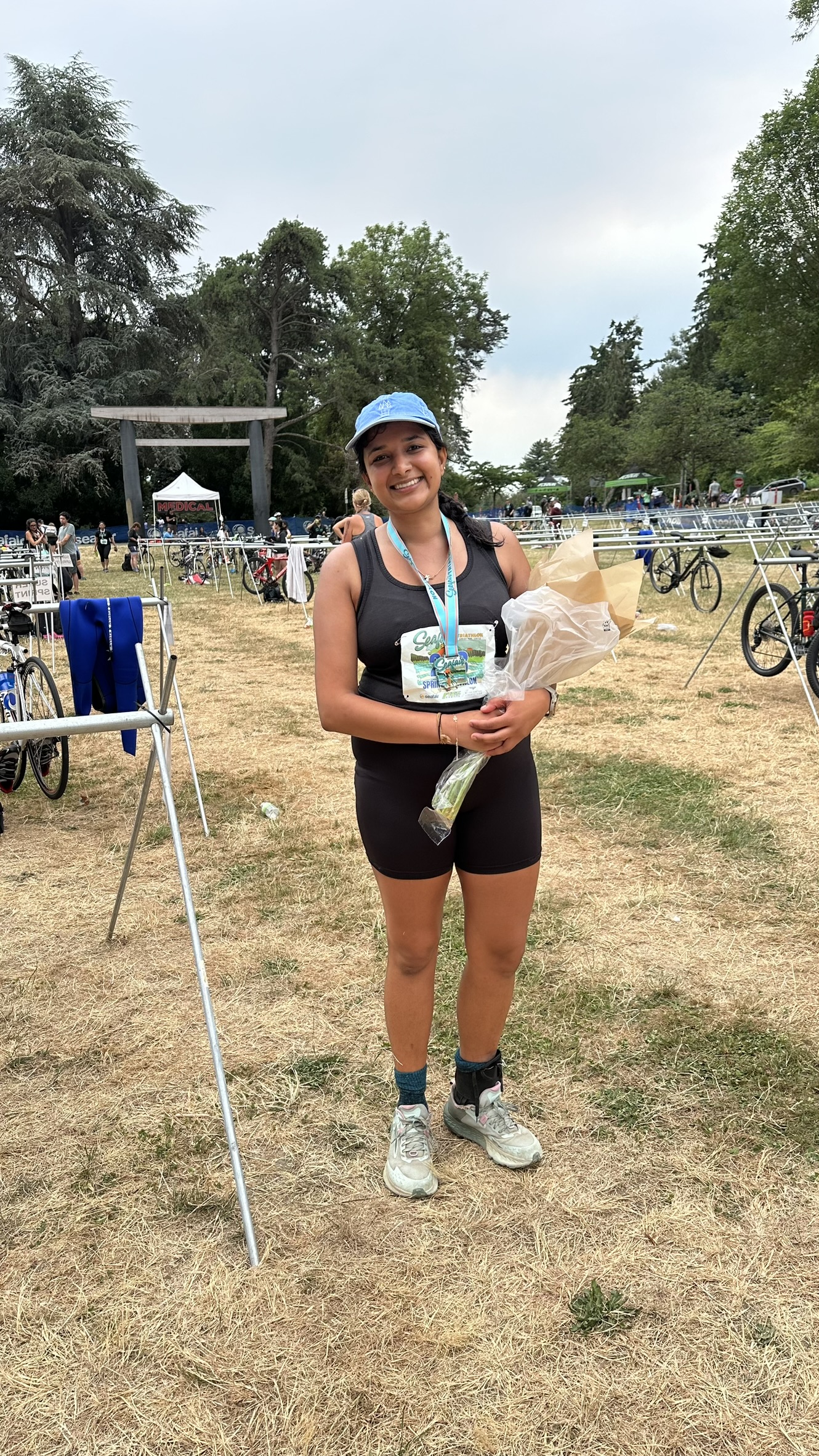 Saachi post-finish with finisher medal, smiling, triathlon gear, transition area behind