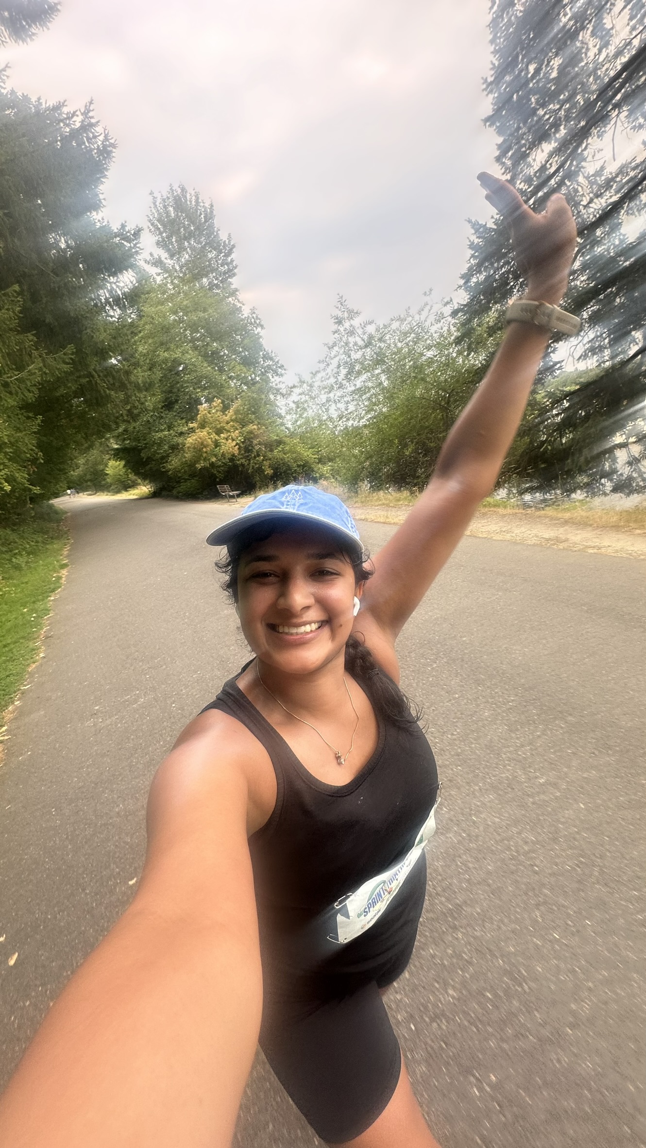 Saachi mid-race selfie on the run course at Seward Park, race bib on, arm raised, big smile